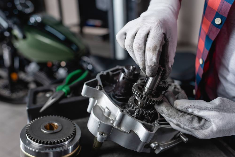 partial view of technician in gloves examining disassembled motorbike gearbox